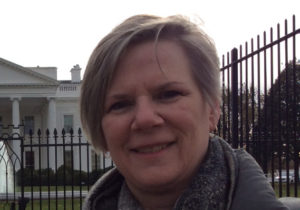 A woman with short hair smiles with the White House in the background.