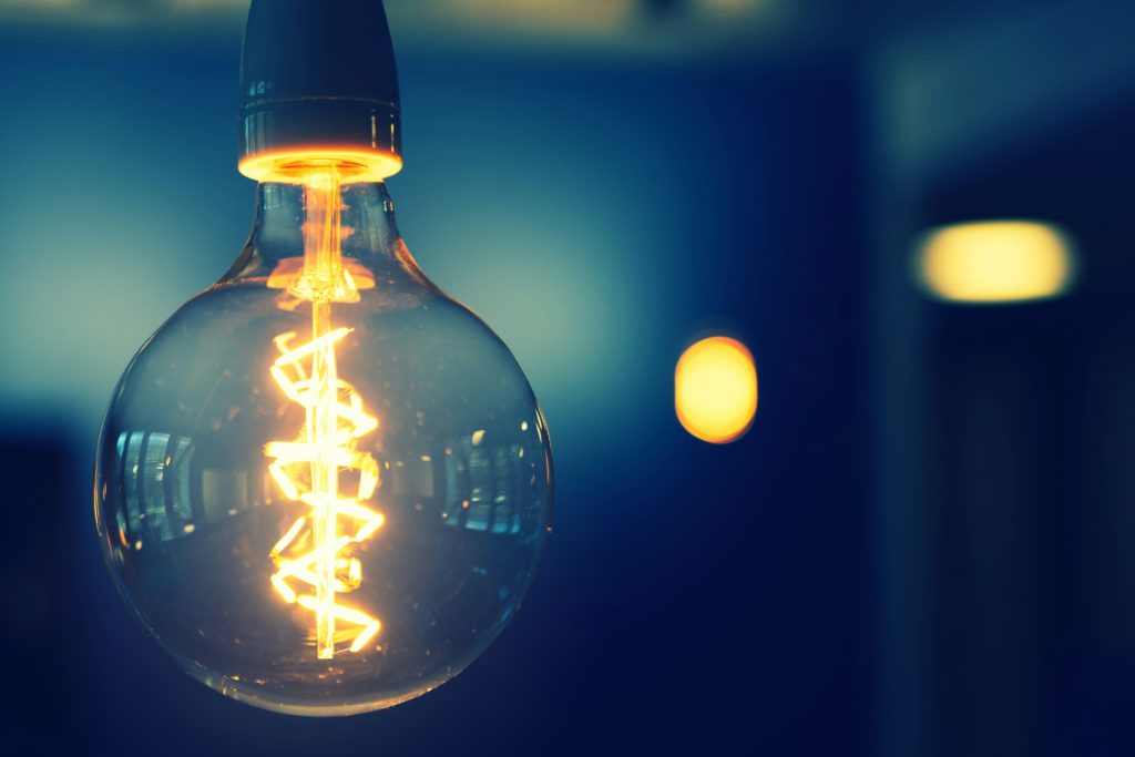 A bright lightbulb that is hanging in a dark room.